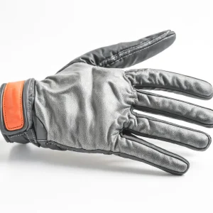 A close-up shot of a black leather glove with orange accents on a white background. The glove is lying on its side, with the palm facing the camera. The glove has a textured surface and a slightly worn look. The orange accents add a pop of color to the otherwise monochrome design.